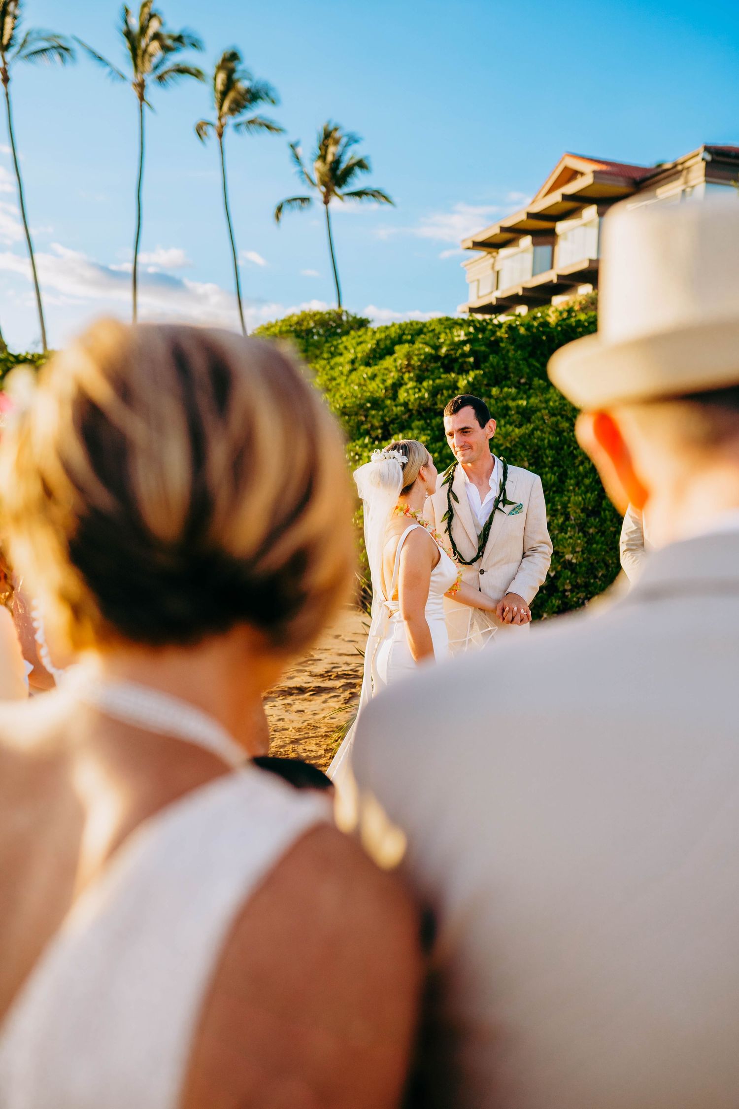 Wedding ceremony guests watch couple exchange vows on tropical beach in Hawaii for beach destination wedding in maui hawaii.