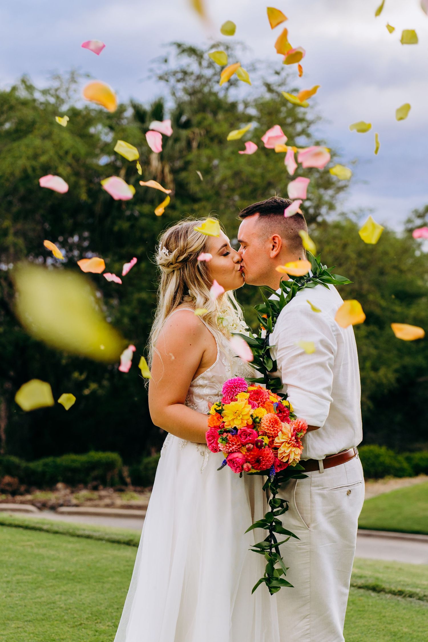 Couple shares romantic kiss during outdoor wedding ceremony with flower petals falling. Maui Hawaii Wailea Kihei Gather on Maui wedding