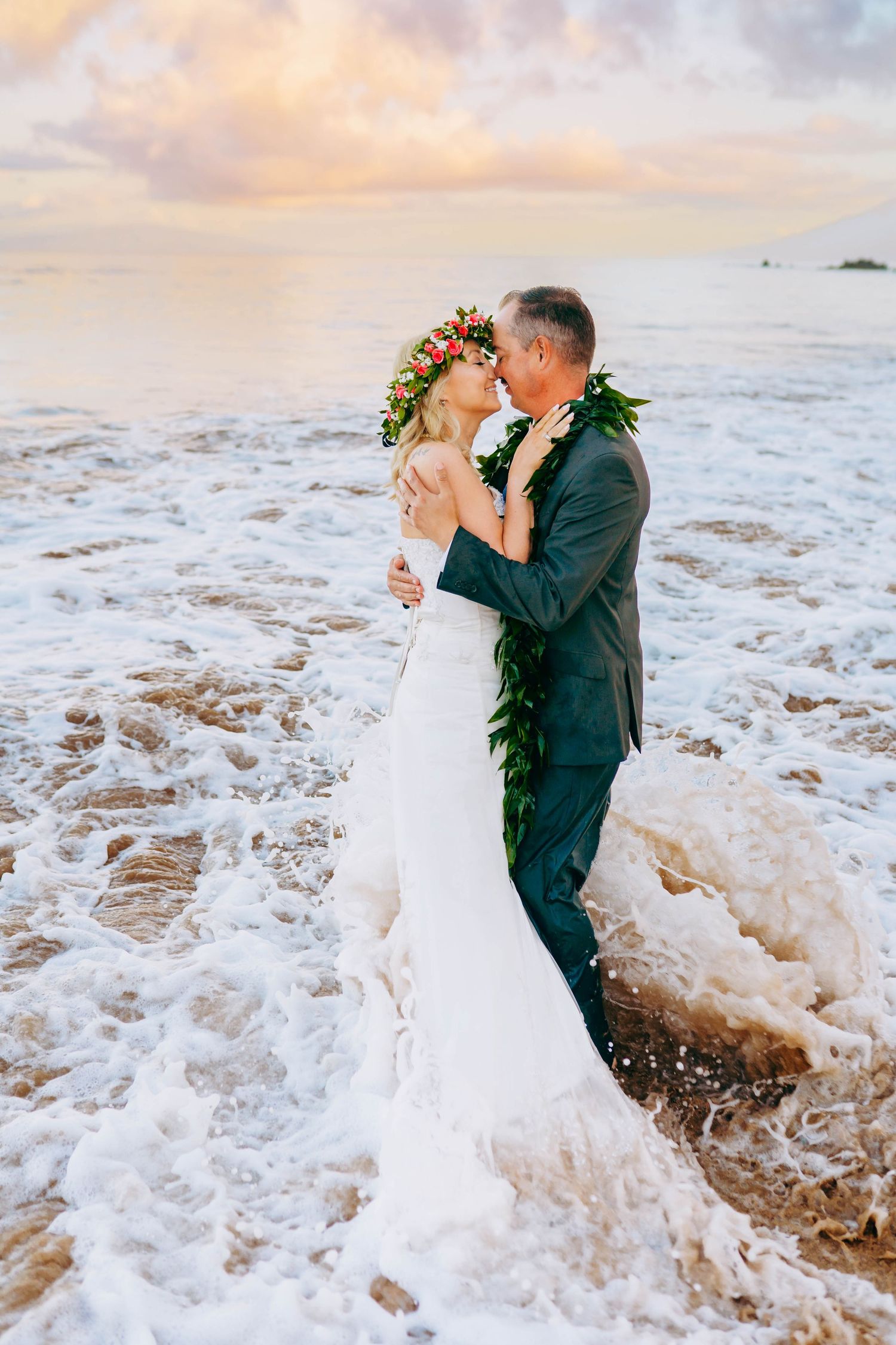 Newlyweds embrace in crashing waves during sunset beach wedding in Hawaii for beach destination wedding in maui hawaii.