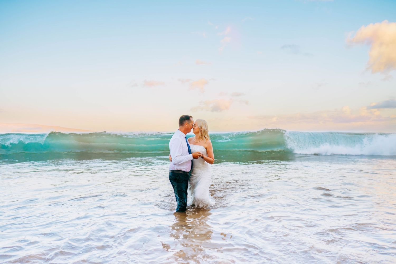 Romantic couple in wedding attire walking through ocean waves at sunset in Hawaii for beach destination wedding in maui hawaii.