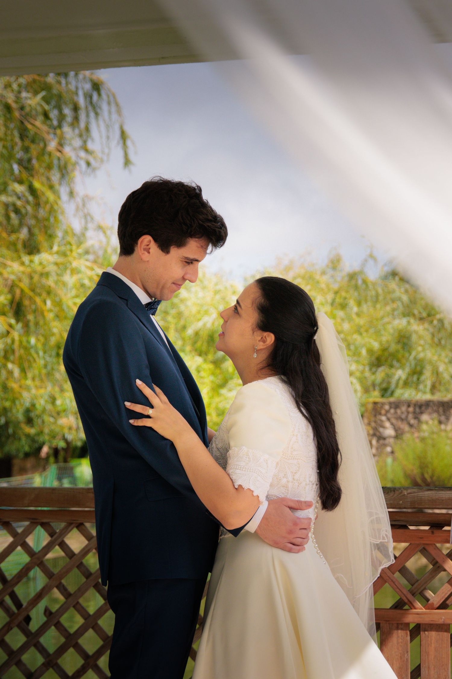 A tender embrace between newlyweds under a garden pergola with soft natural lighting.