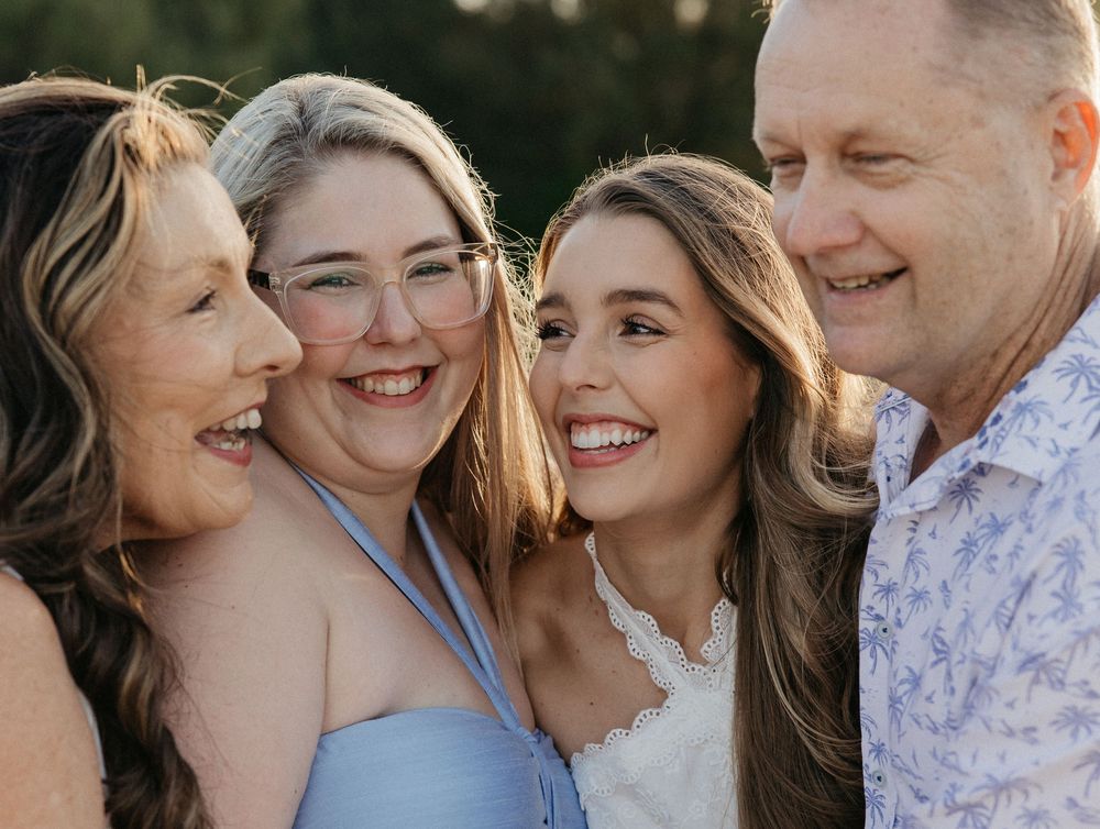 A happy family of four smiling closely together outdoors, featuring two women and an older couple in a warm portrait.