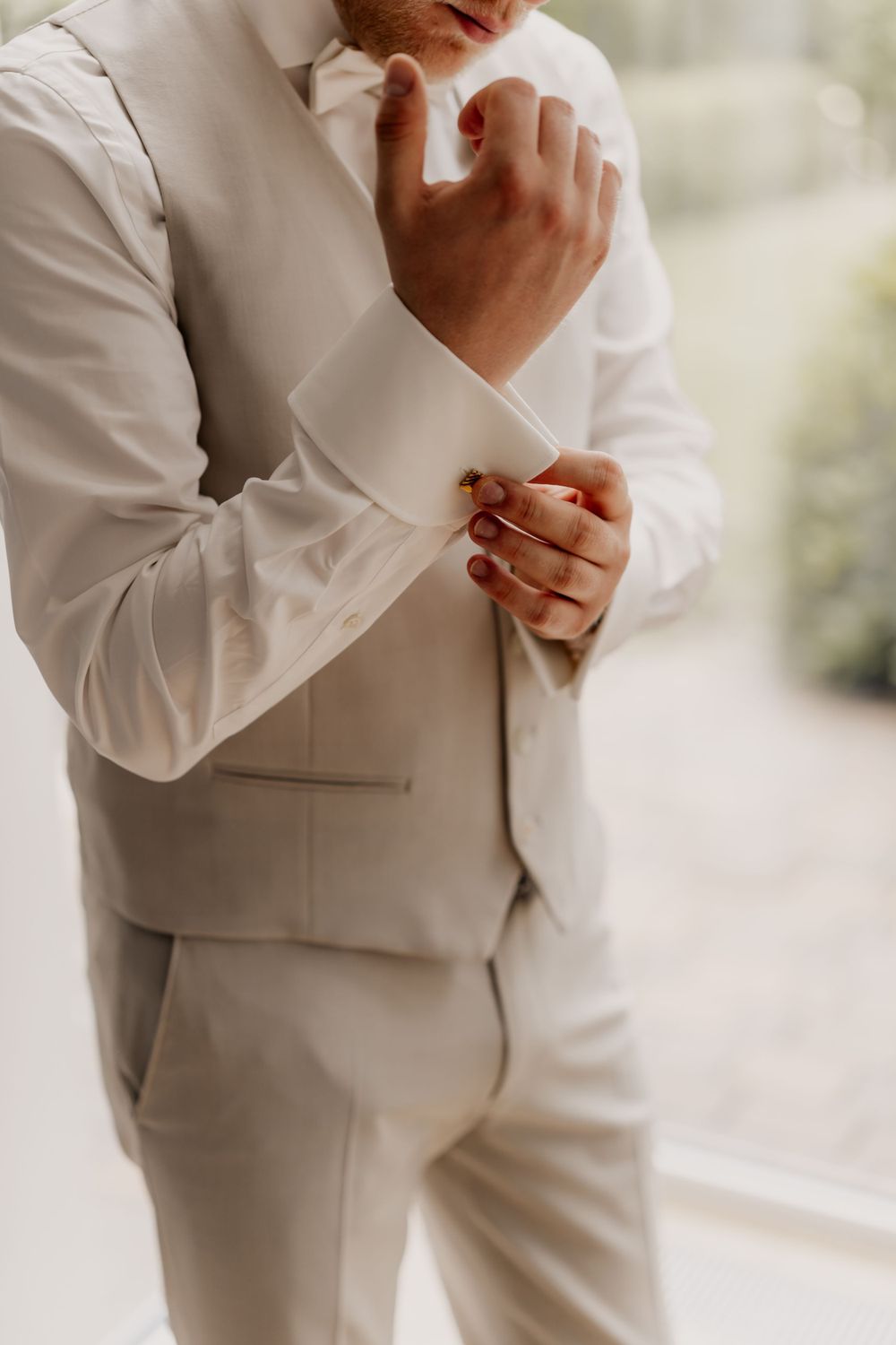 Close-up of hands adjusting white suit cuff links and sleeve preparation.