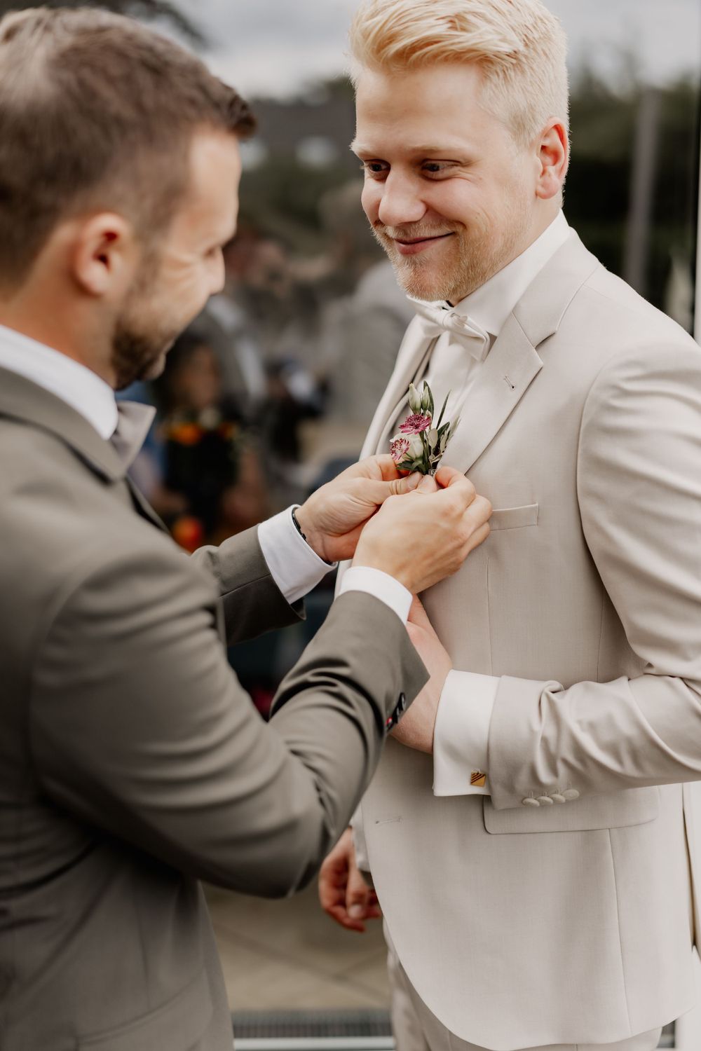Two people in formal attire adjusting a boutonniere during a wedding ceremony.
