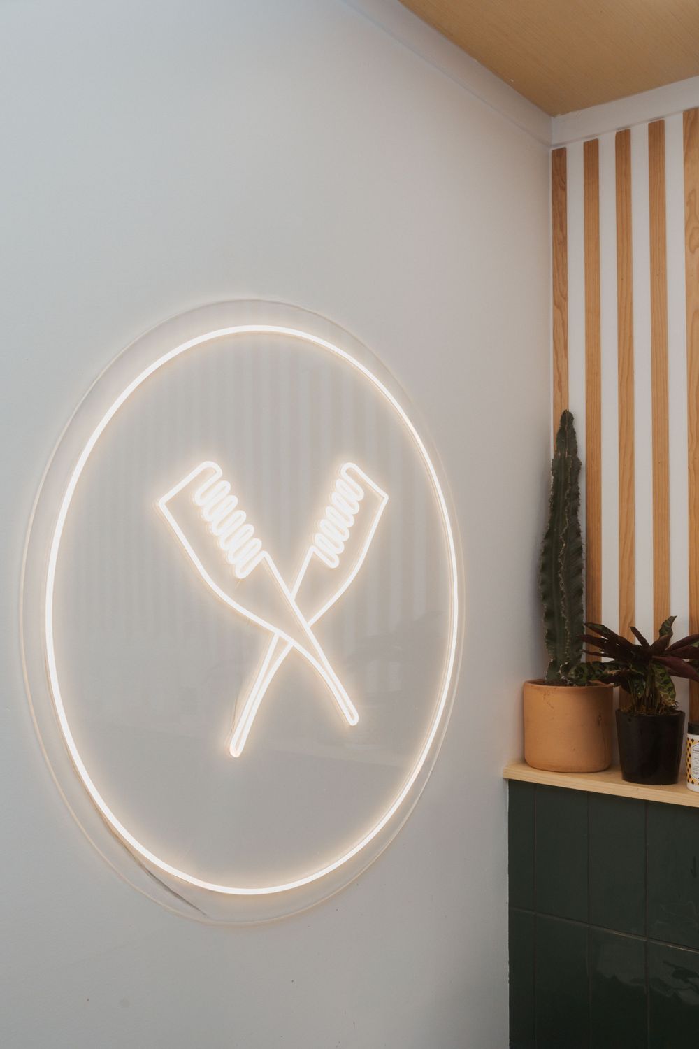 Neon light sign showing crossed hair brushes in a circle against wood-paneled wall.