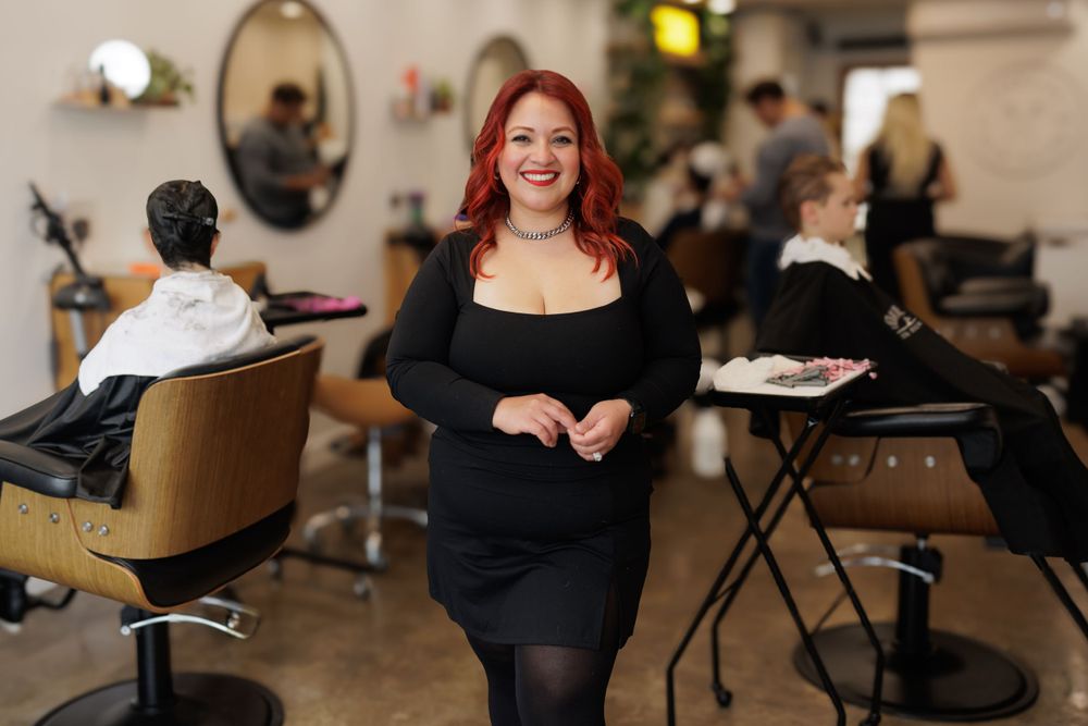 Professional hairstylist standing confidently in a salon wearing all black attire.
