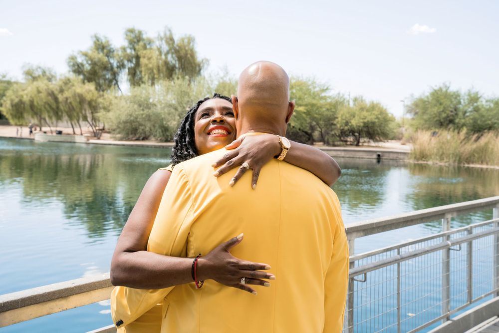 Couple in yellow outfits sharing intimate embrace by lakeside with railing.