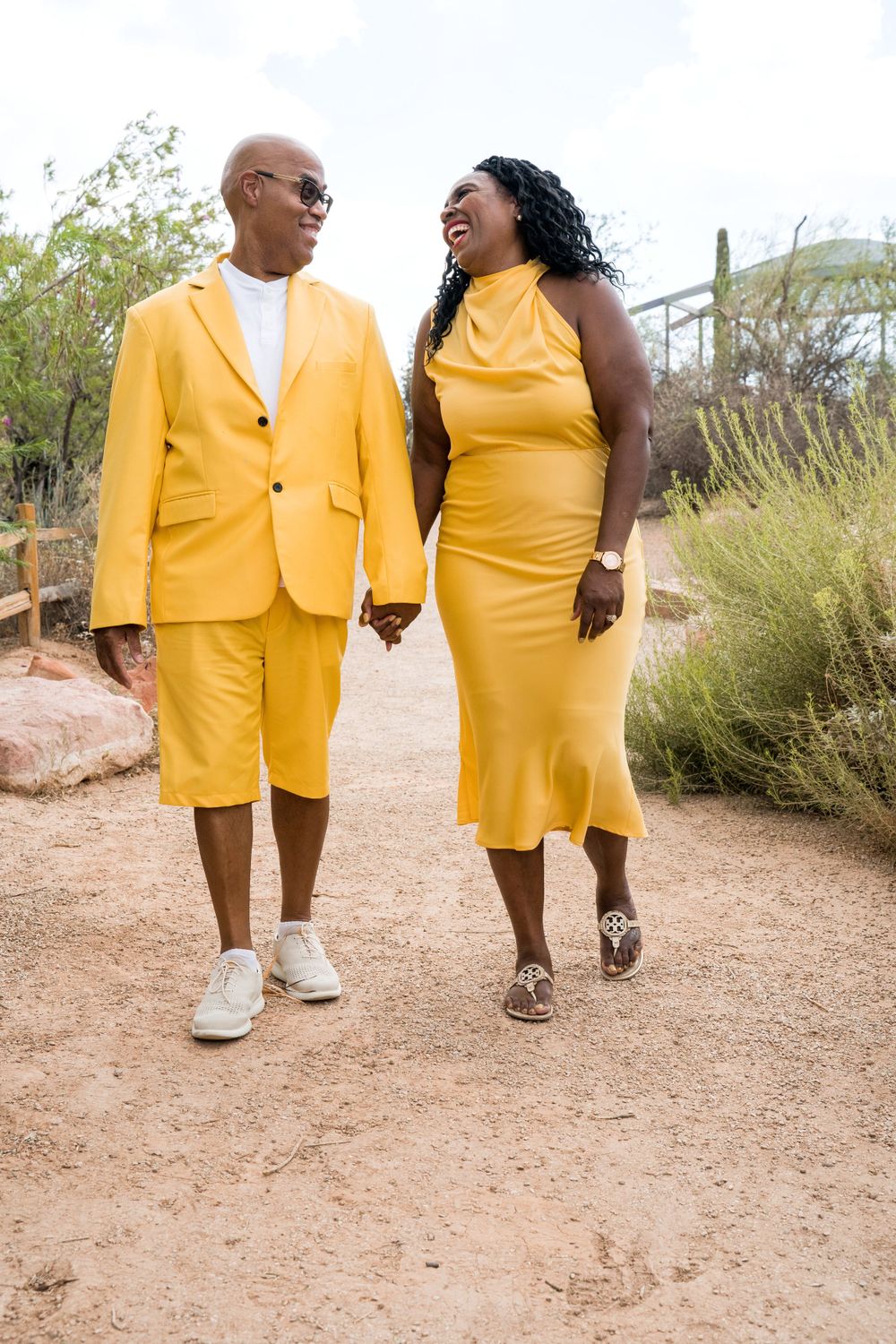Stylish couple in bright yellow attire walking together on desert trail.