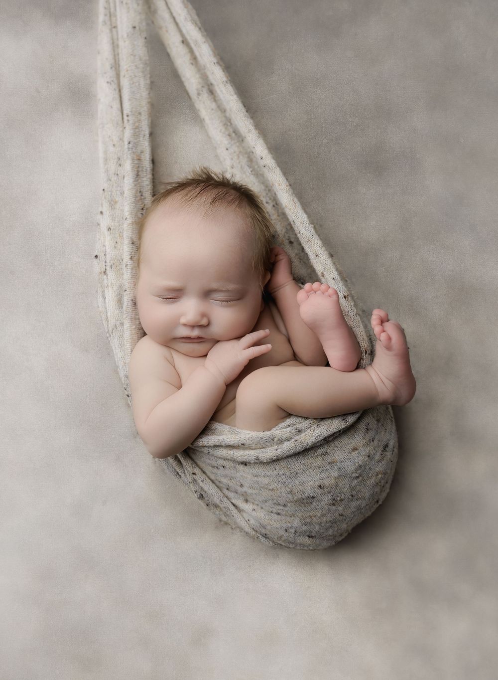 Newborn portrait in signature hammock pose with neutral tones, sleeping peacefully in studio