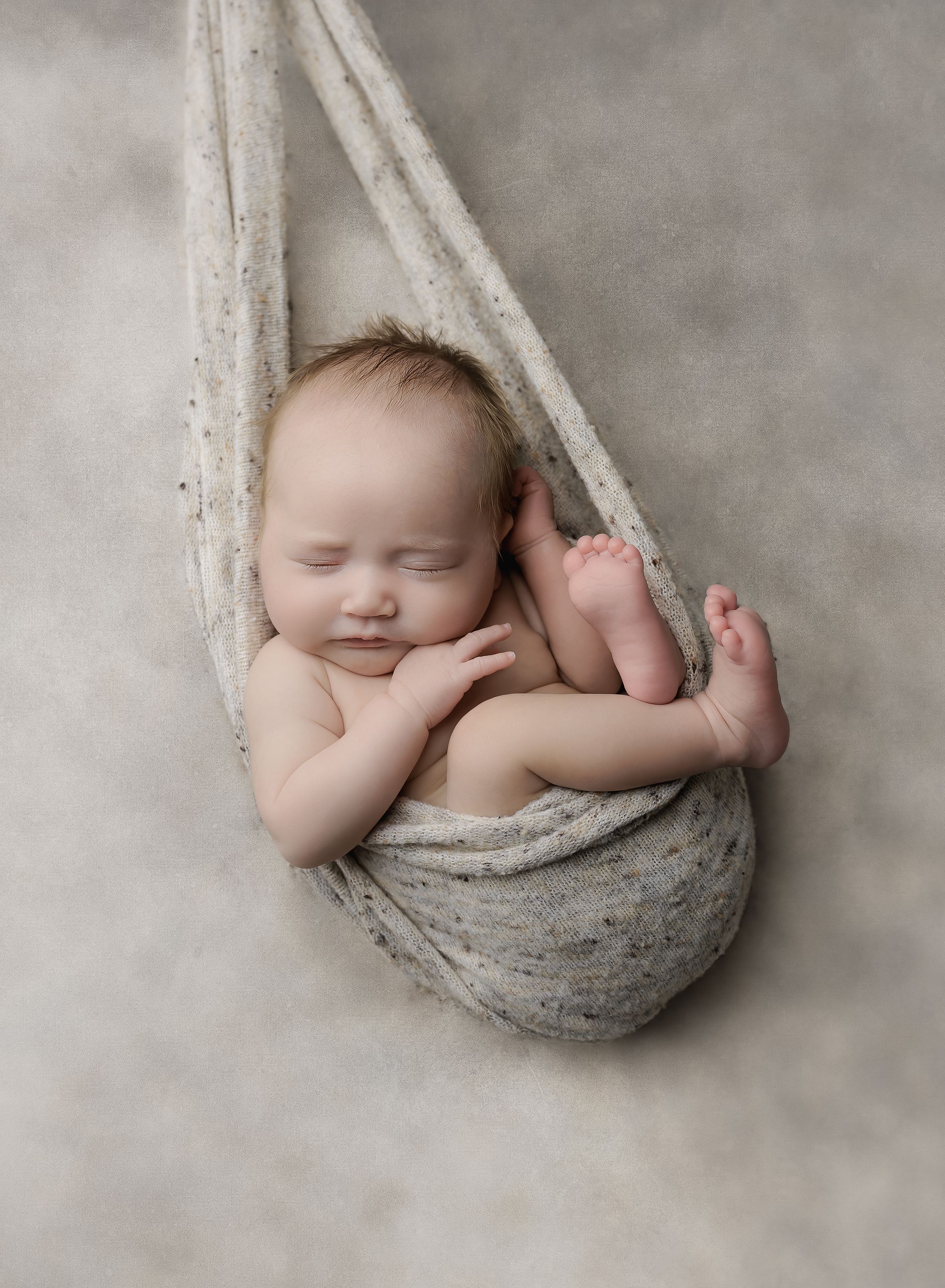 Newborn portrait in signature hammock pose with neutral tones, sleeping peacefully in studio