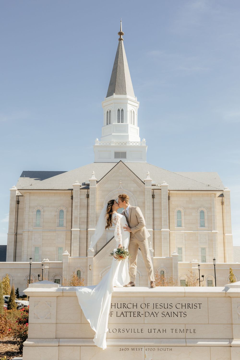Newlyweds kissing on temple sign wall at Taylorsville Utah LDS Temple wedding.