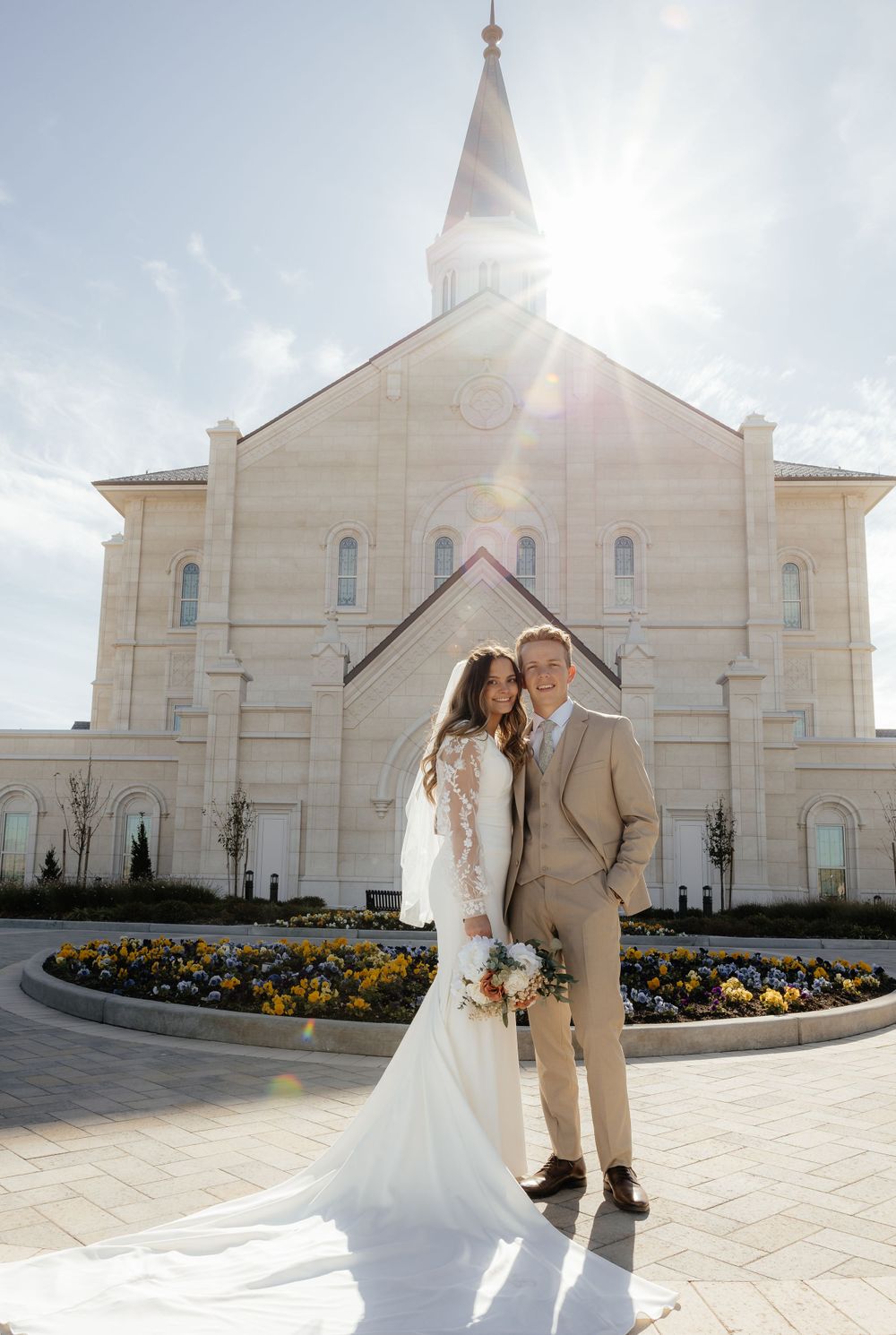 Bride and groom posing before Taylorsville Utah Temple with sun flare overhead.