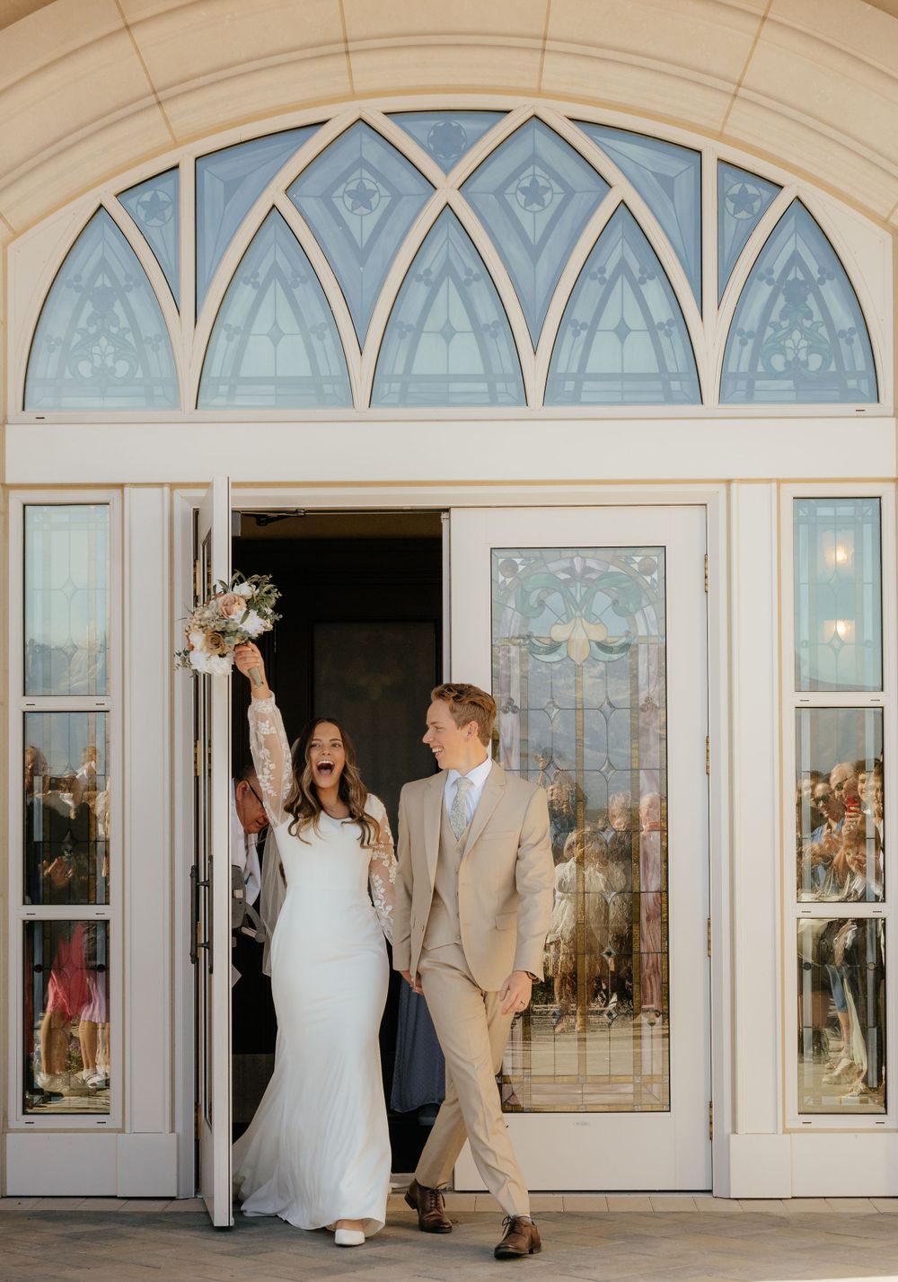Bride and groom exiting church doors celebrating their wedding with bouquet raised.