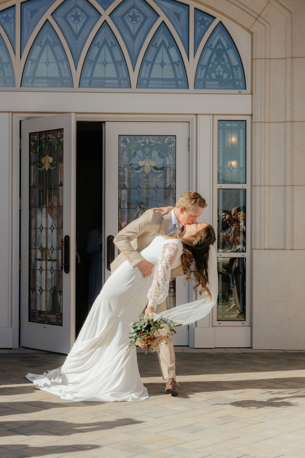 Groom dipping bride for a romantic kiss outside LDS temple doors on wedding day.