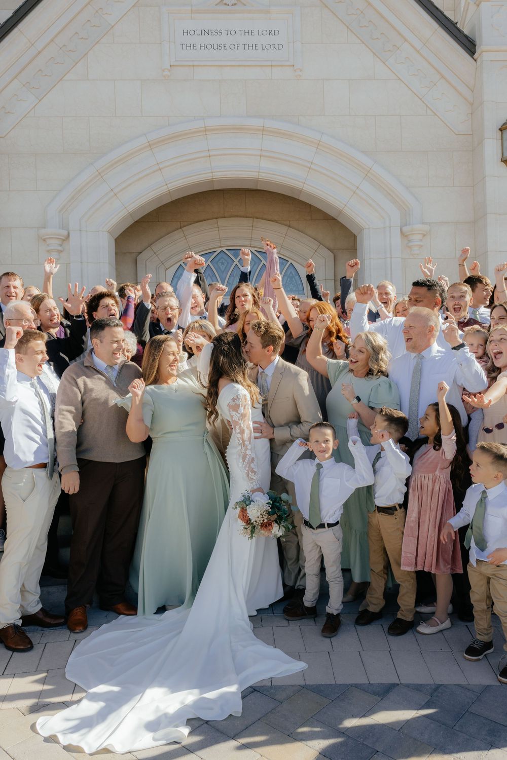 Large wedding party celebrating with raised hands outside Taylorsville Utah Temple.