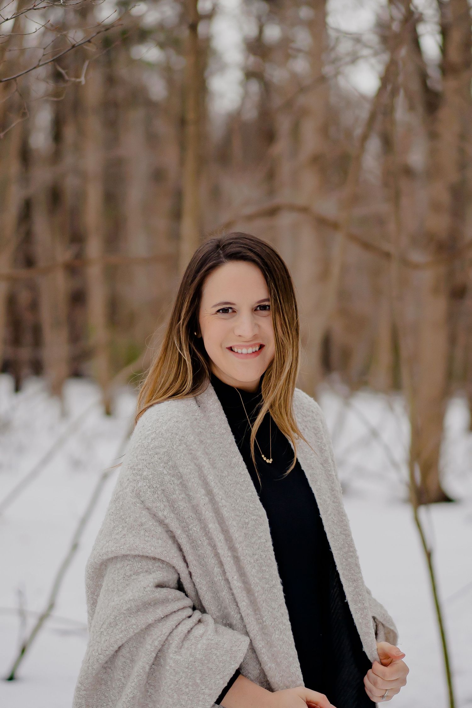 Portrait of woman in beige cardigan standing in snowy winter forest.