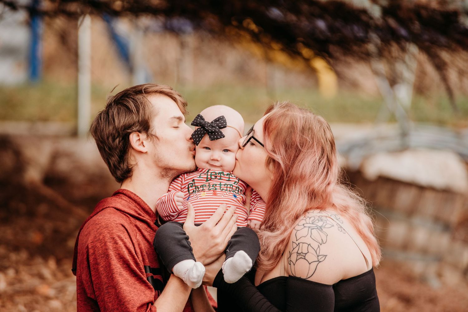 Parents kissing their baby's cheeks in a sweet family moment outdoors.