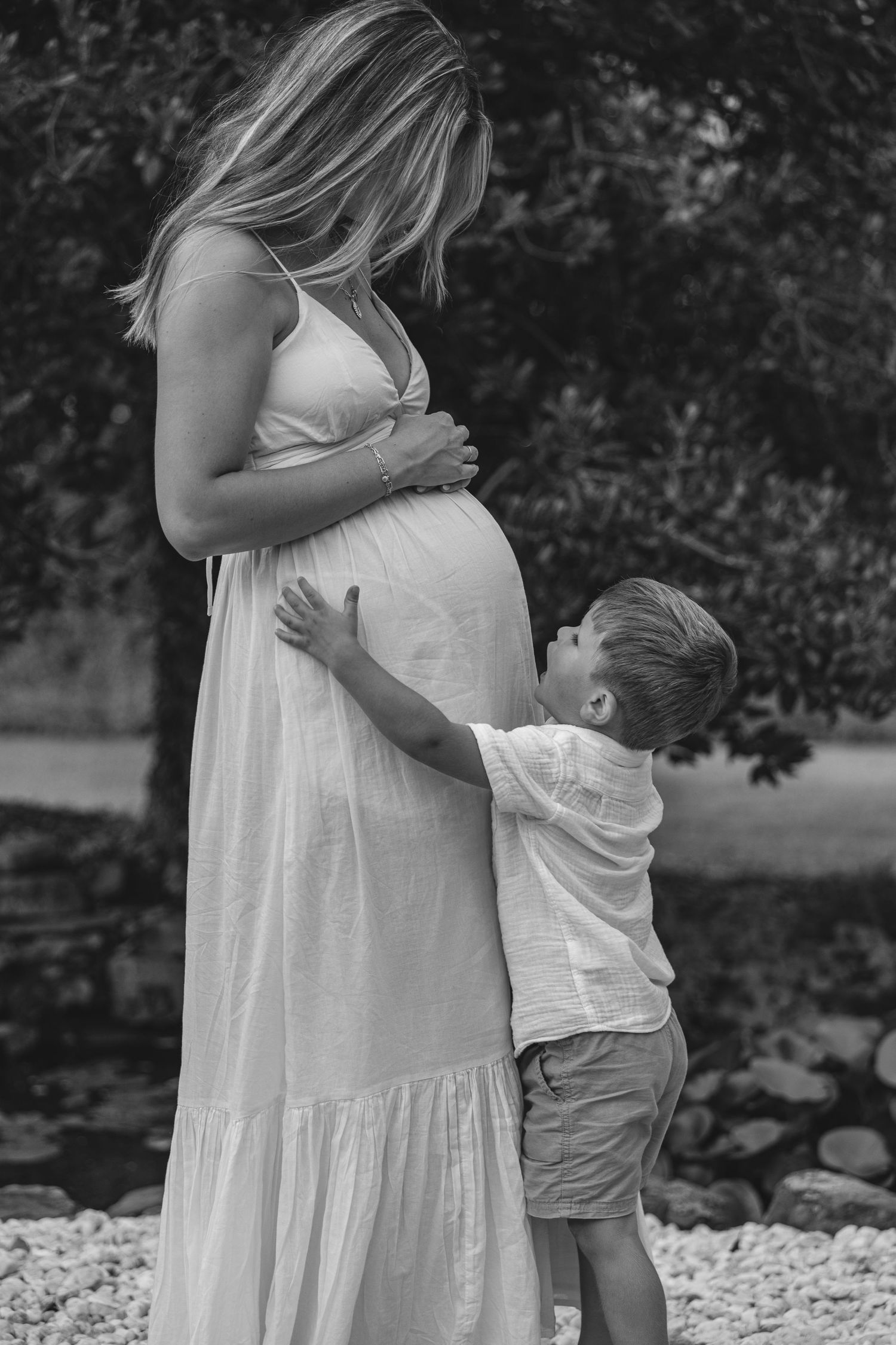 Hands form heart shape over pregnant belly in flowing red dress.