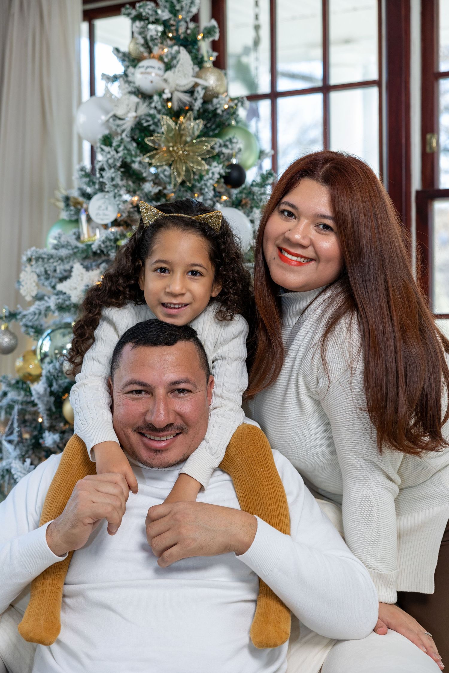 Beautifully decorated Christmas tree with family in white sweaters sitting together for holiday photo.