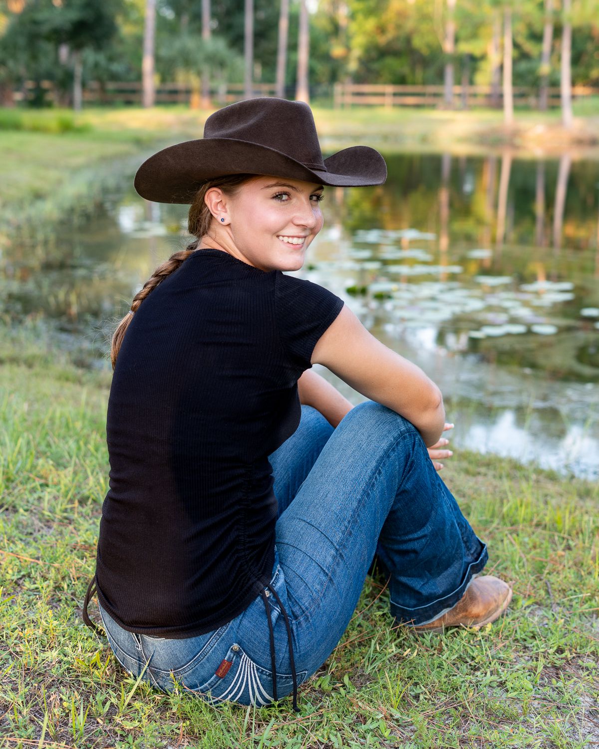 A person in a black shirt and jeans sits by a tranquil pond in a series of relaxed outdoor poses.