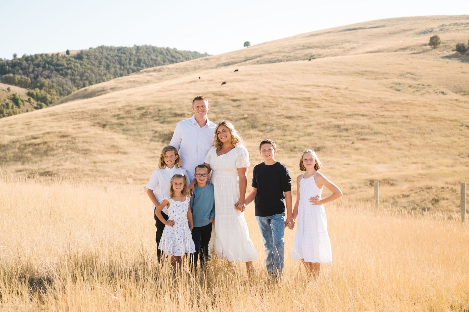 A family poses together in a golden meadow with rolling hills in the background.