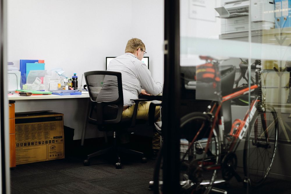 Modern office desk setup with computer monitor and bicycle visible in background.