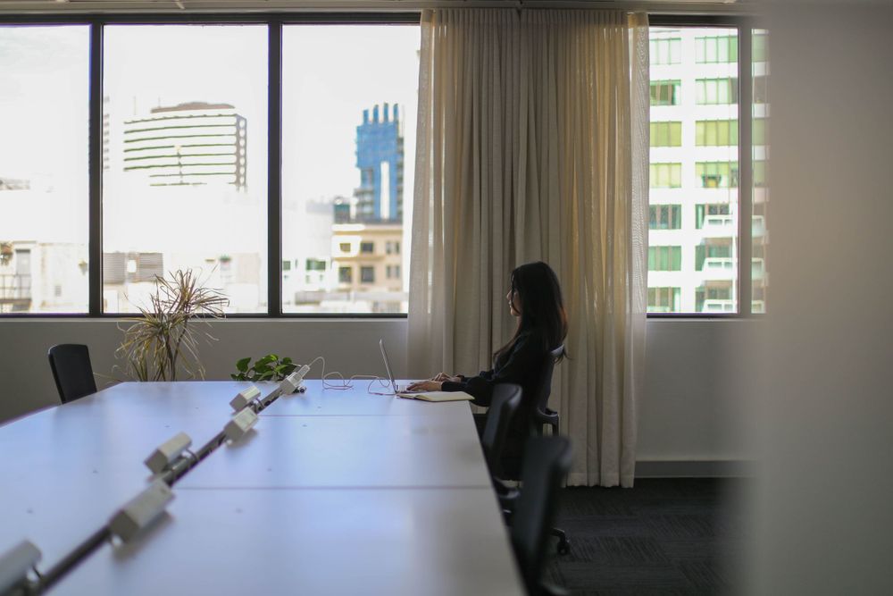 Minimalist conference room with long white table and city view through large windows.