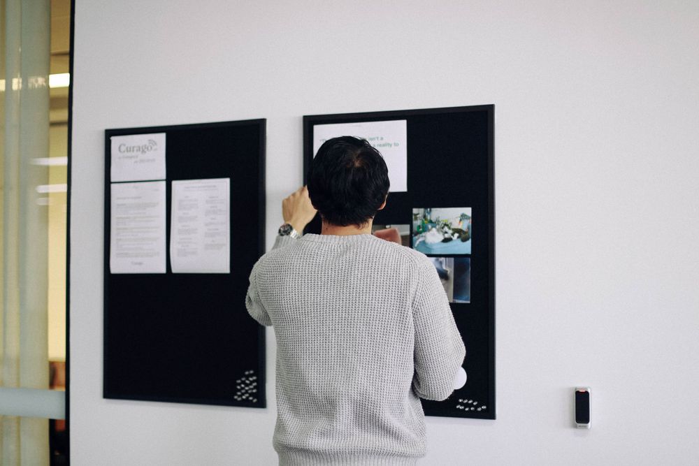 Office bulletin board with documents and notices mounted on white wall.