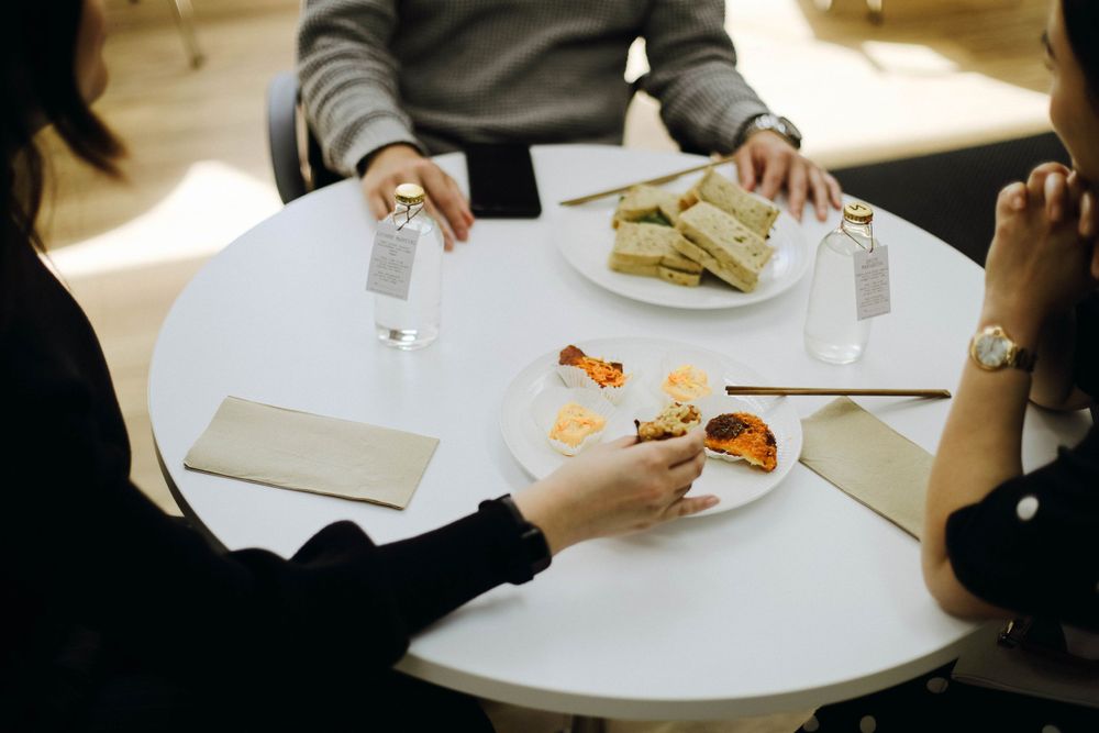 Overhead view of people sharing snacks and drinks at a white table.