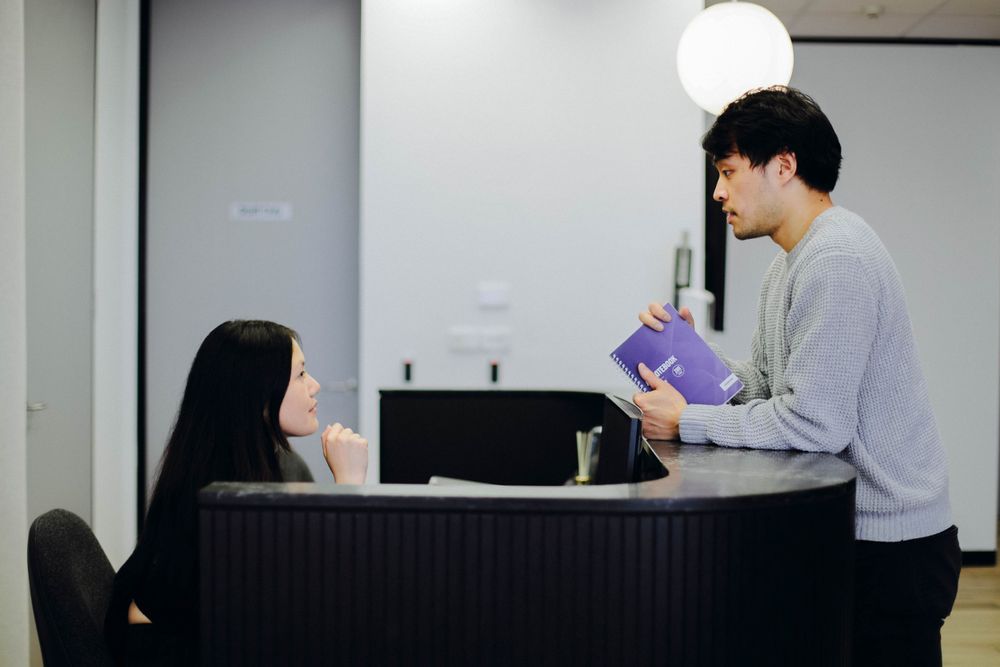Two people having a conversation at an office reception desk.
