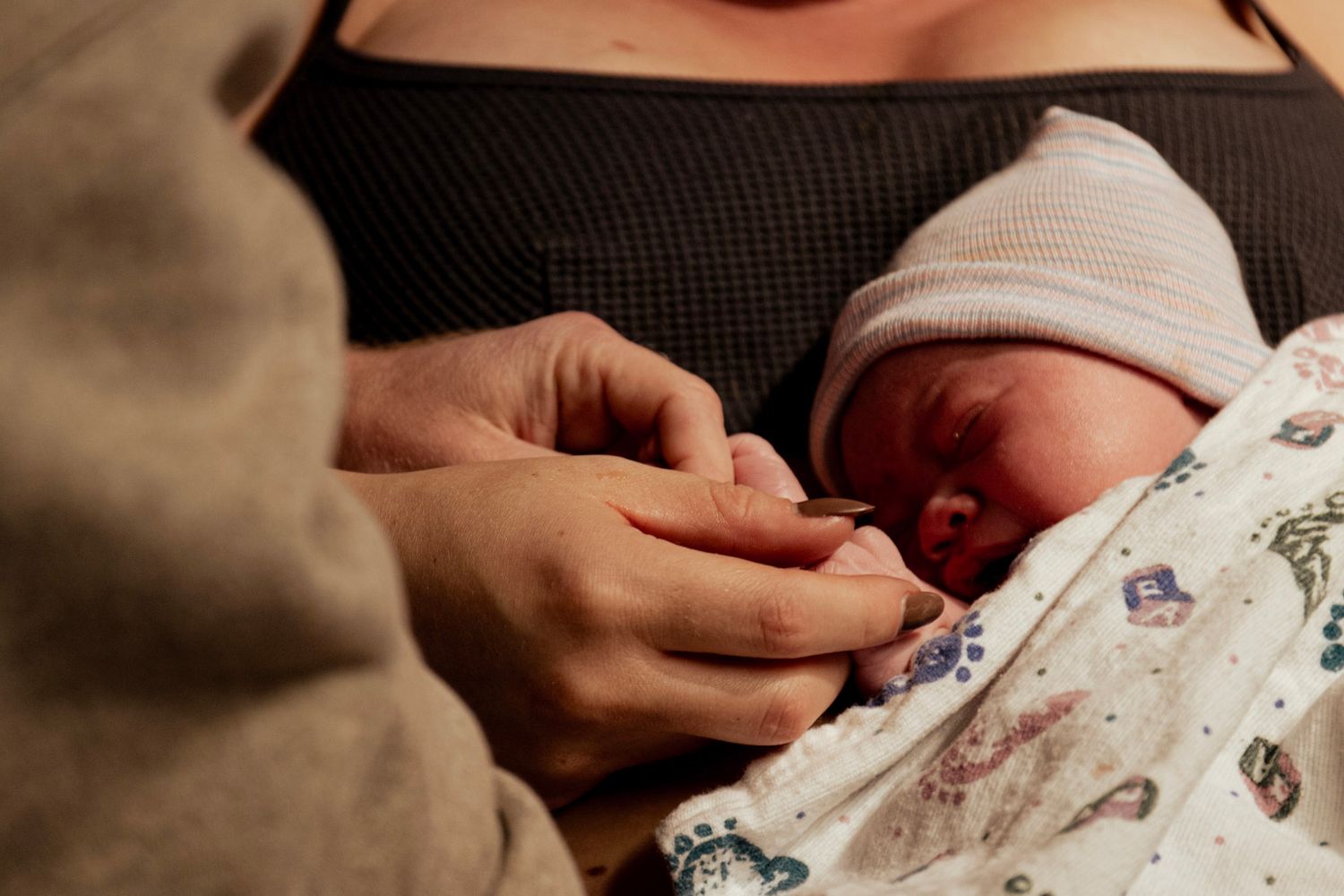 Gentle hands holding and caring for a newborn baby wearing a knit cap.