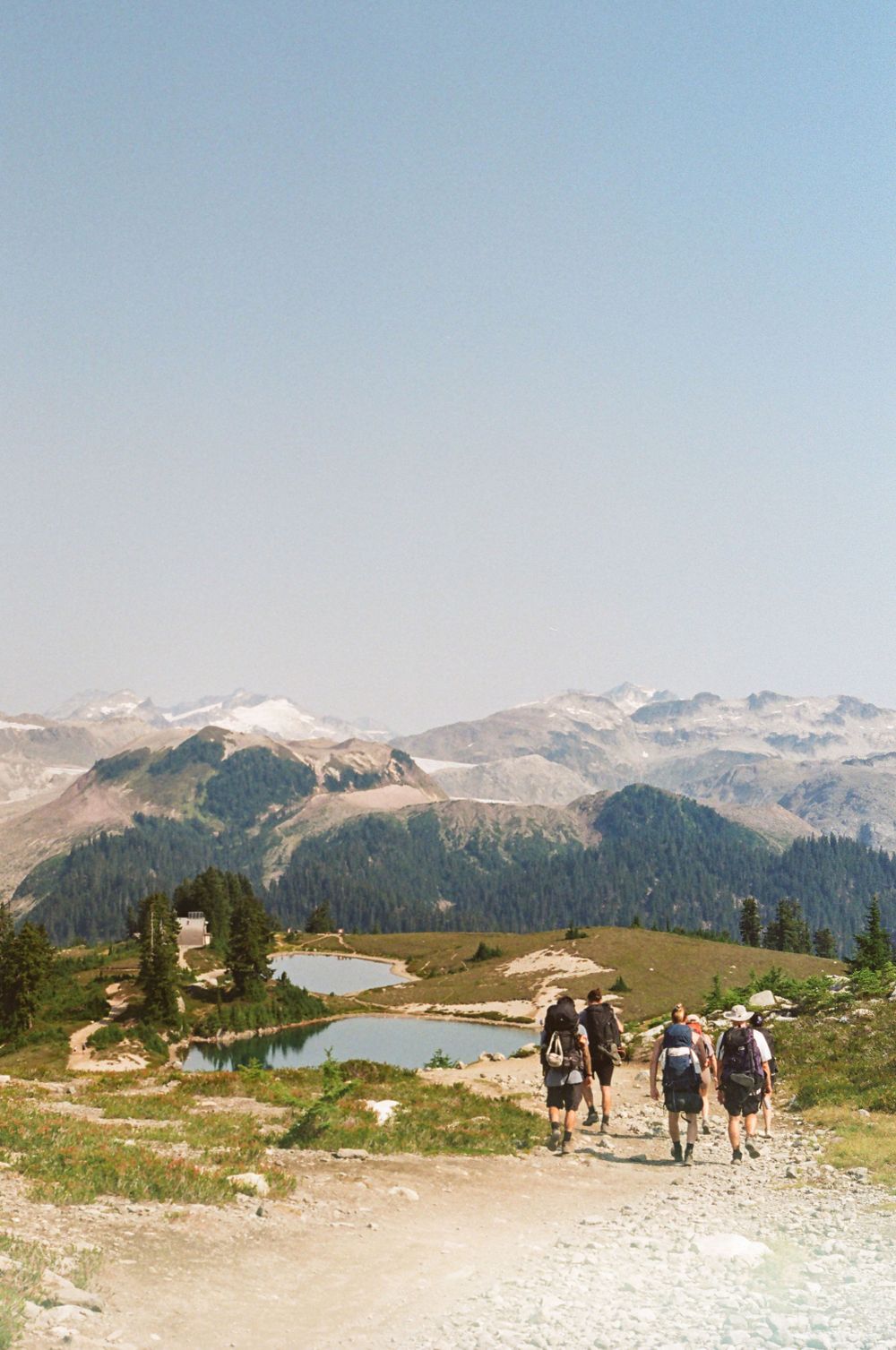 Panoramic view of alpine lakes and mountain peaks from a rocky hiking trail.