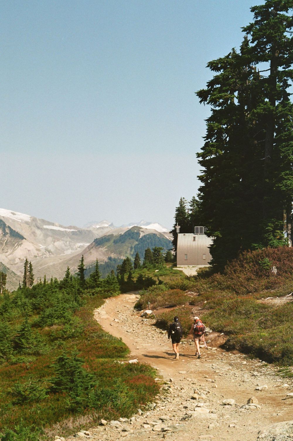 Rocky mountain hiking path winding through alpine terrain with distant snow-capped peaks.