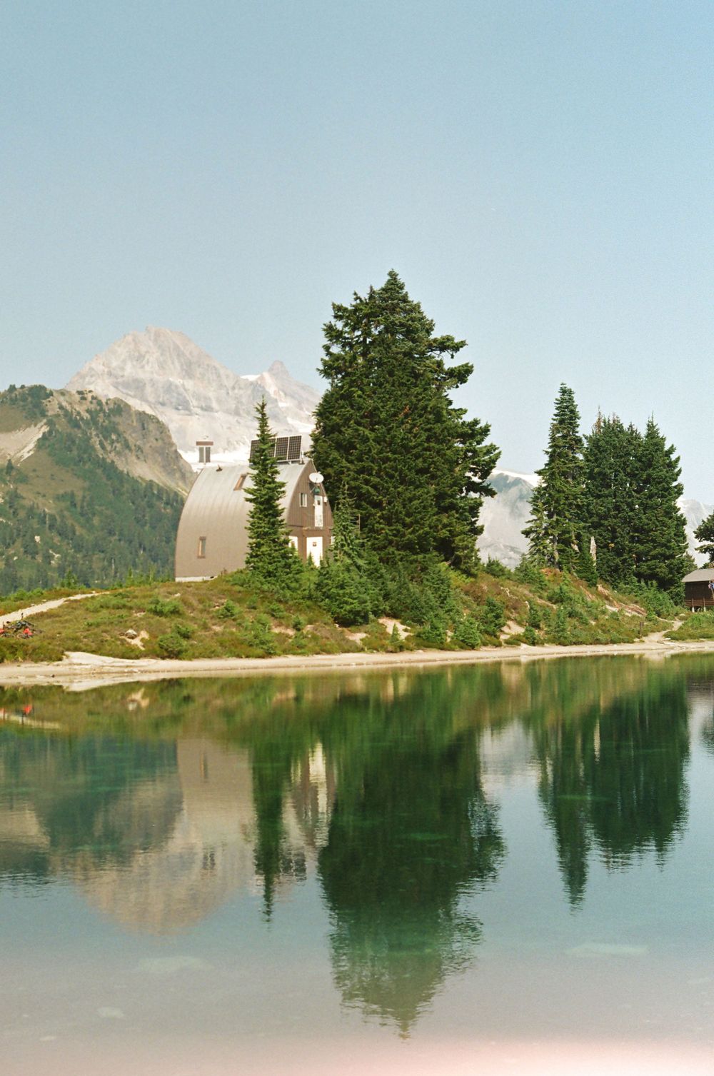 Tranquil alpine lake reflecting evergreen trees and mountain peaks in crystal clear water.
