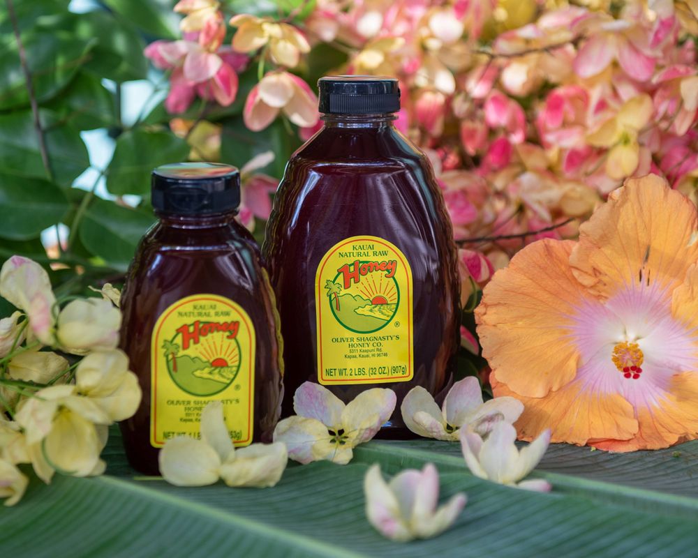 Two bottles of honey syrup arranged with tropical flowers and leaves.