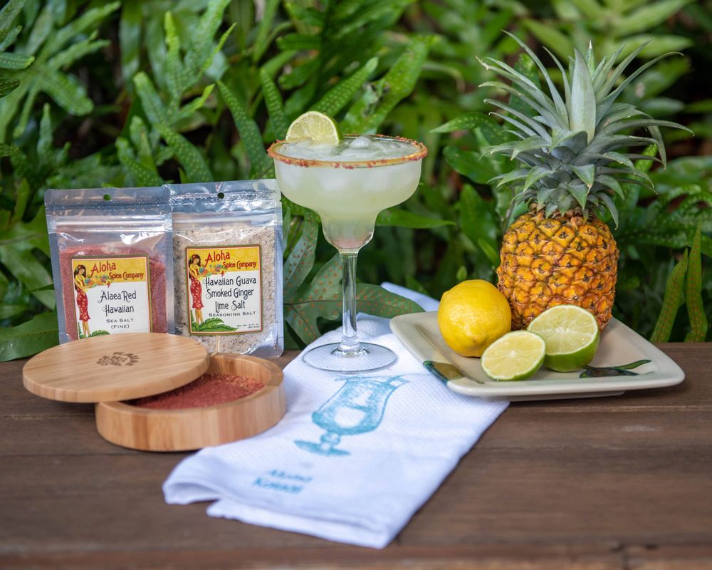 Margarita cocktail setup with pineapple, limes and drink mix packets on wooden table.