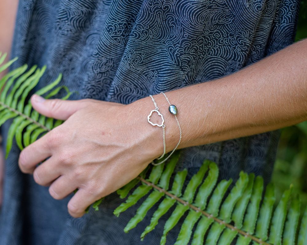 Silver bracelet with geometric charm design worn against tropical fern background.