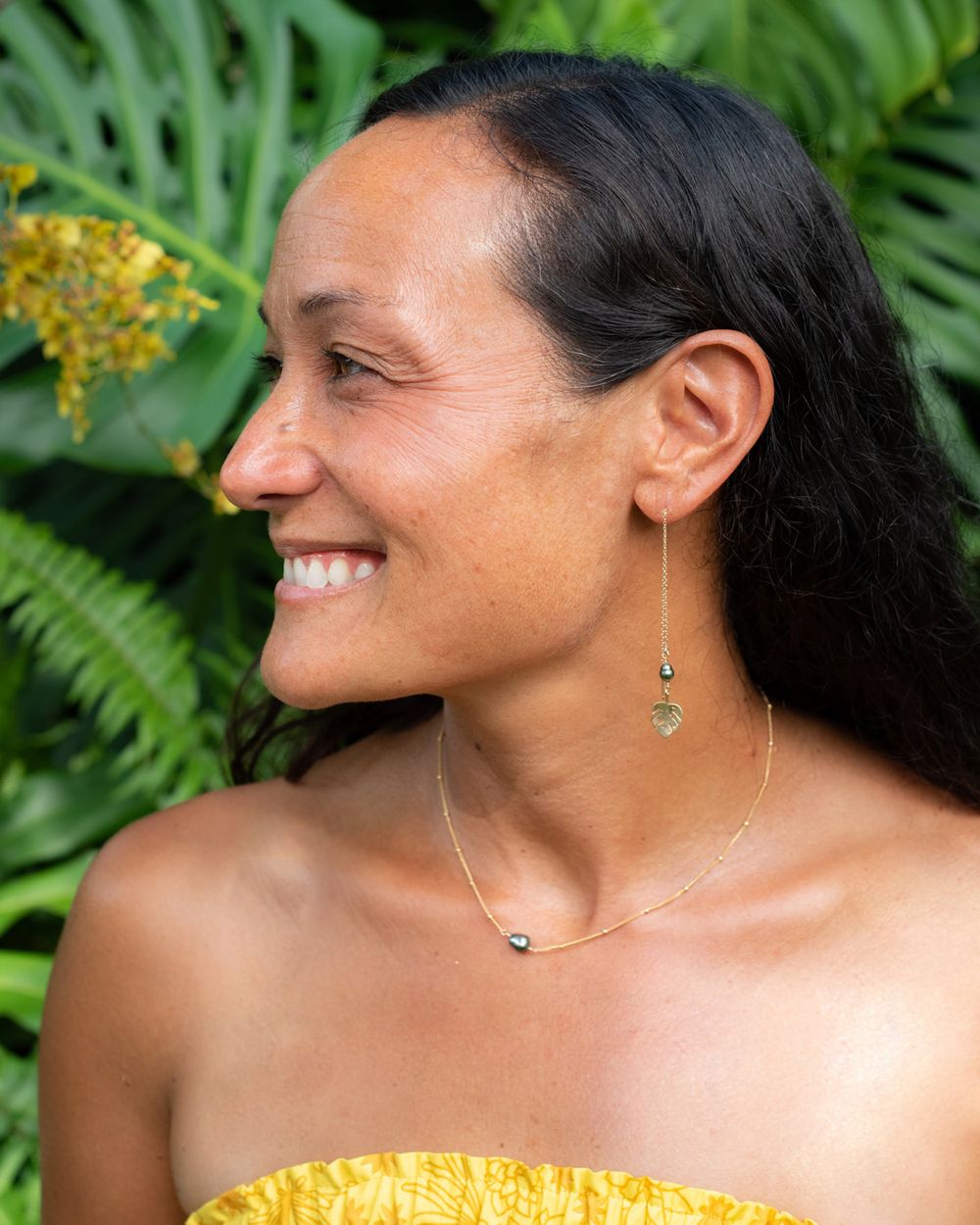 Handcrafted tropical jewelry styled with a yellow top against lush green foliage.