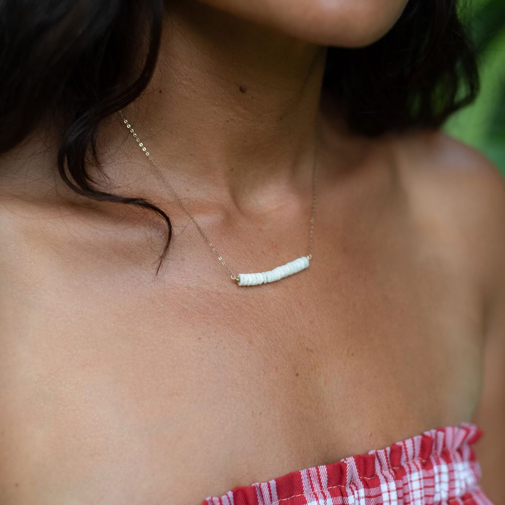 Minimalist white bar necklace worn with a red and white patterned top.