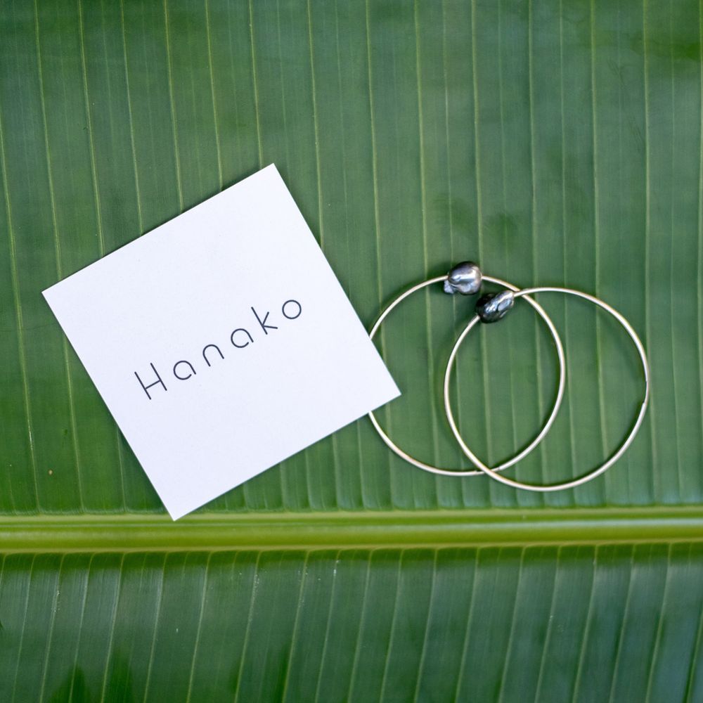 Hanako branded circular hoop earrings displayed on white card against green palm leaf.