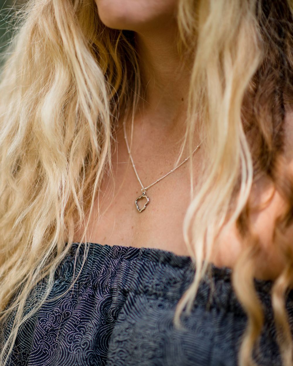 Delicate silver necklace worn with dark textured dress against blonde hair.