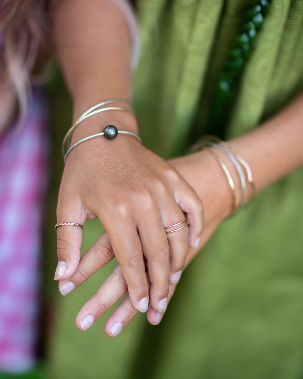 Close-up of hands wearing minimalist silver jewelry against green background.