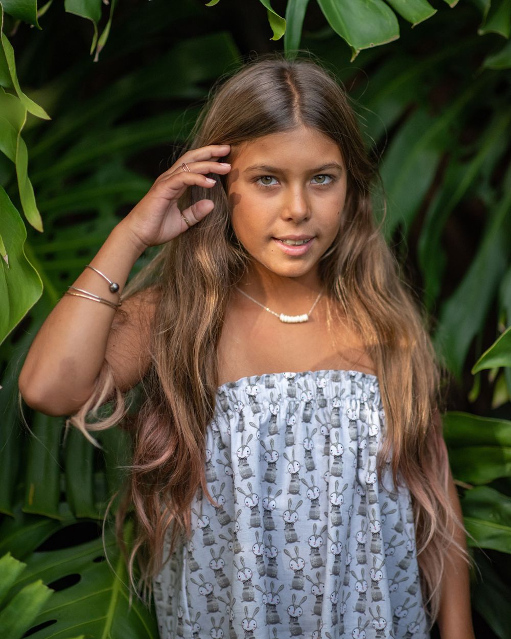 Portrait in tropical setting wearing white patterned dress and delicate necklace.
