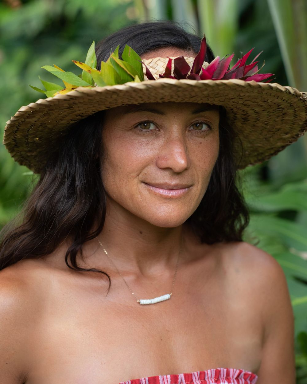 Woman wearing straw hat decorated with tropical flowers in nature setting.