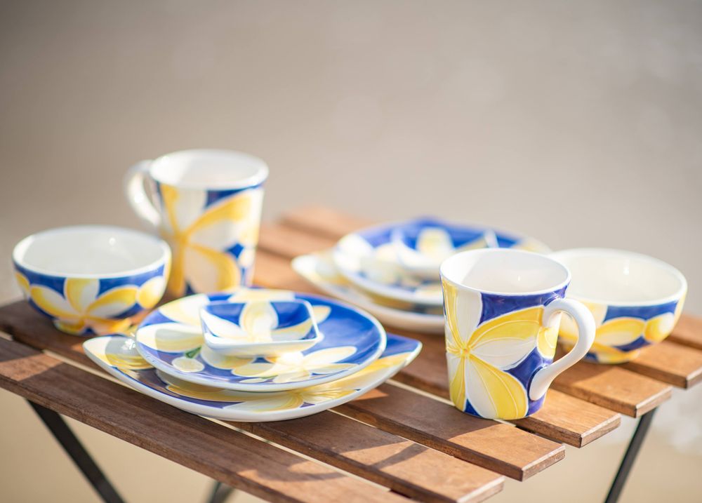 Blue and yellow plumeria-patterned dinnerware set displayed on wooden table.