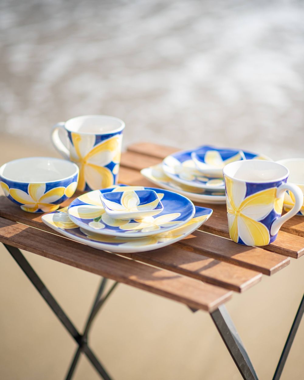 Hawaiian-style blue and yellow floral dinnerware set arranged on wooden folding table.