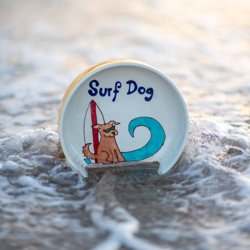 A cute illustration of a surfing dog on a round badge in ocean water.