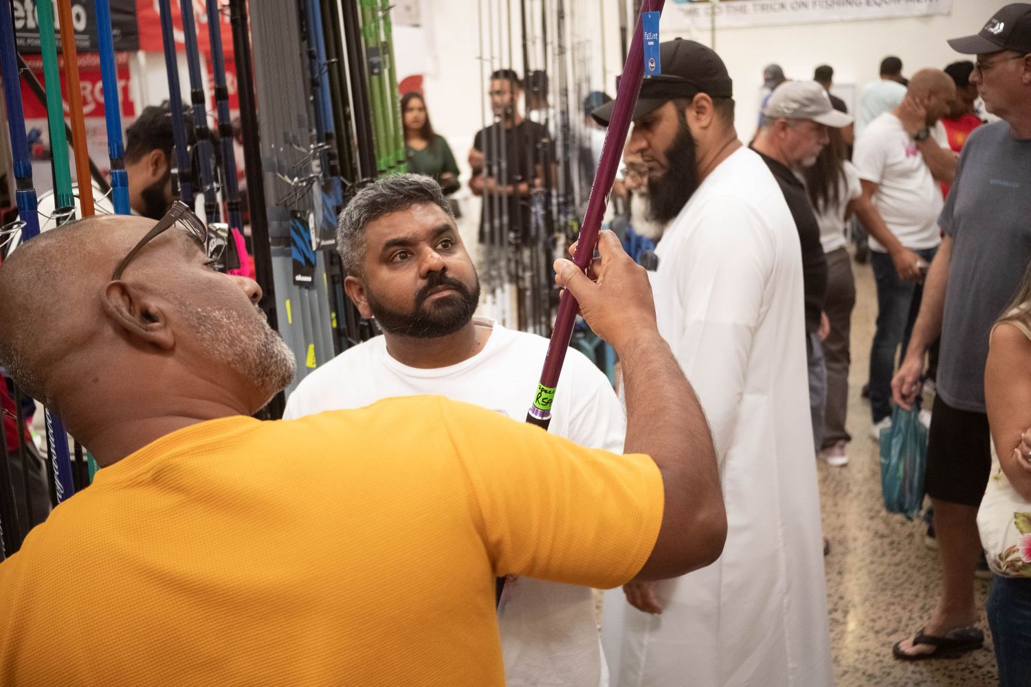 Group of people examining fishing gear at an outdoor event.