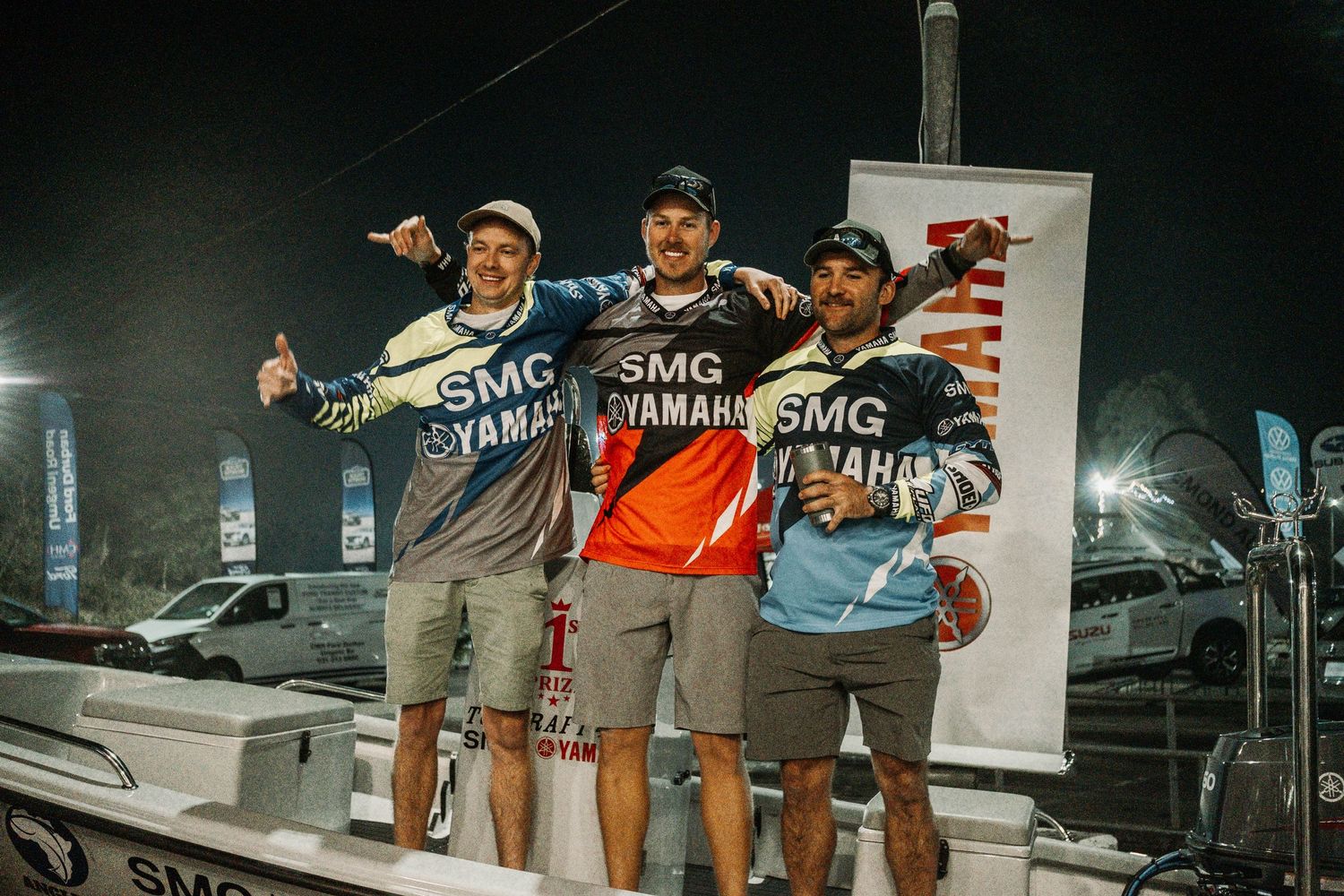 Three tournament winners celebrating on stage with thumbs up gestures.