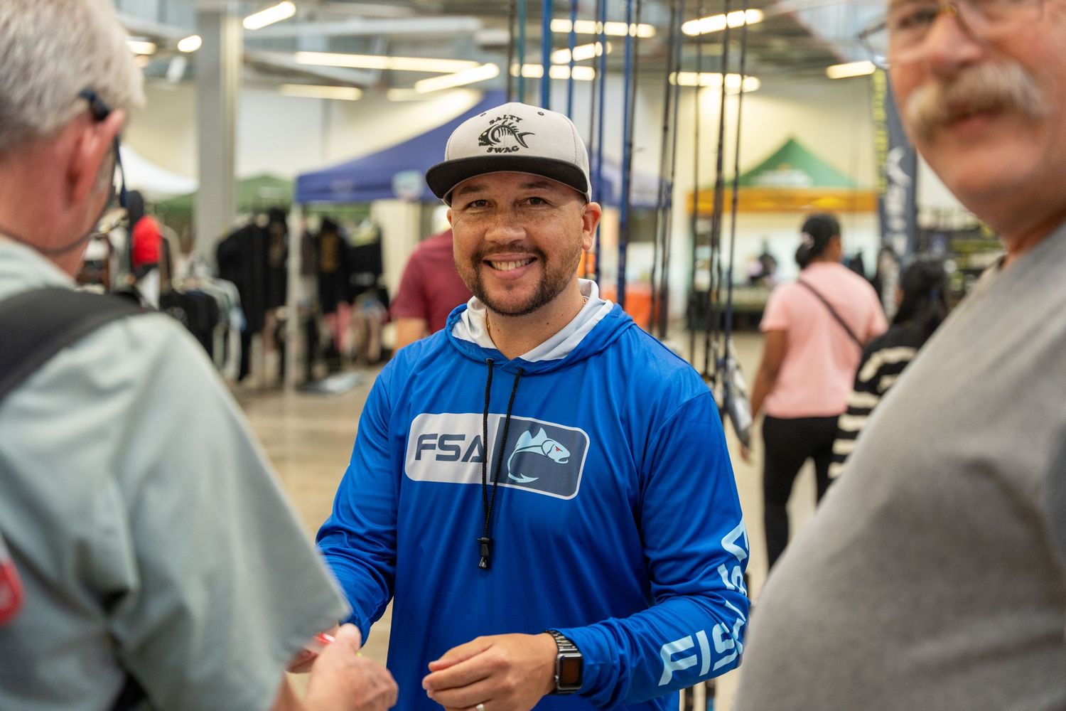 People gathered at an indoor event wearing casual clothing and baseball caps.